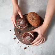 Homemade chocolate ice cream in a coconut shell with whole coconut holding womans hands on a gray concrete background with place for text. Summer dessert.