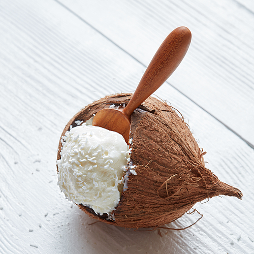 Homemade organic coconut ice cream. An ice cream ball in a wooden spoon in coconut Close up on a white wooden background