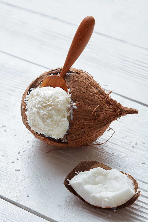Fresh bowl of ice cream in coconut with a wooden spoon on a light wooden background