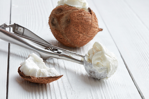 Metal scoop with fresh coconut ice cream on a light wooden background
