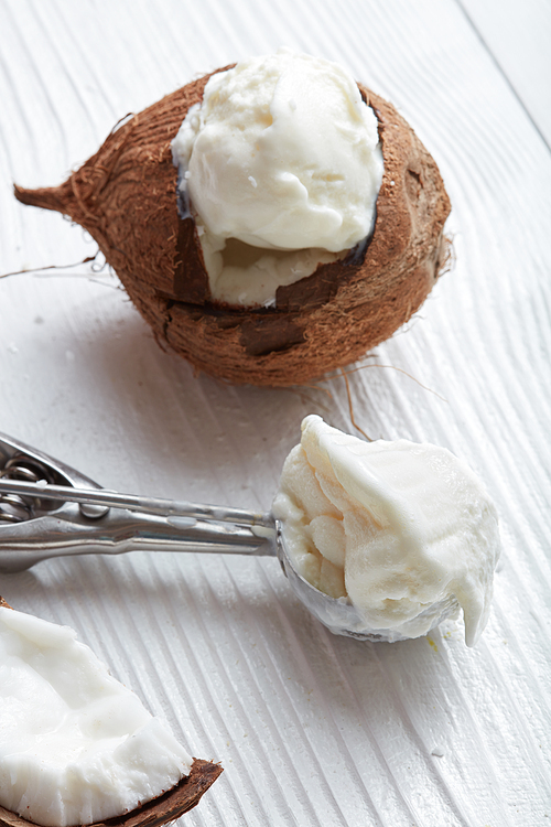 A fresh ice cream in a coconut and a spoon on a white wooden background.close-up