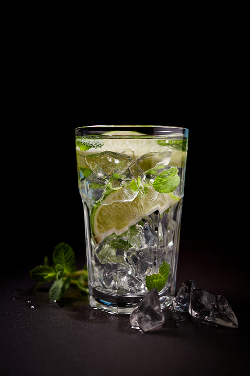Glass of iced lemonade soda with slice lime, ice and mint leaves isolated on black, cold drink in summer