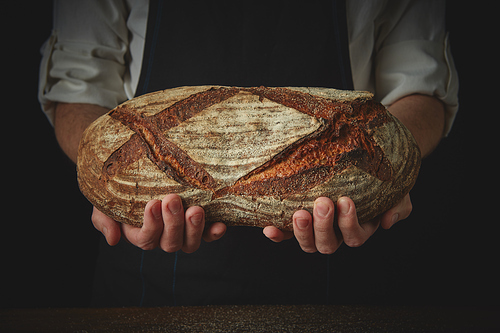 Men's hands hold organic dark bread on a dark background close-up