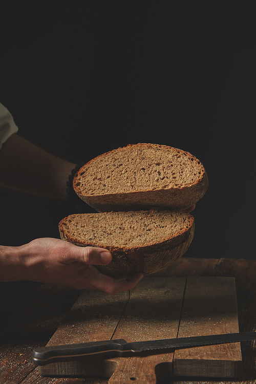the man baker holds in his hands halves of rye bread, against the background of the old brown table