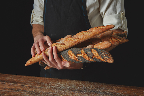 Men's hands hold freshly baked baguettes against the black background of a wooden table