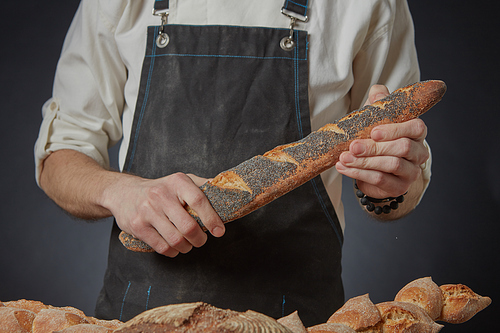 Men's hands holding a fresh baguette with poppy seeds on a dark background clous up
