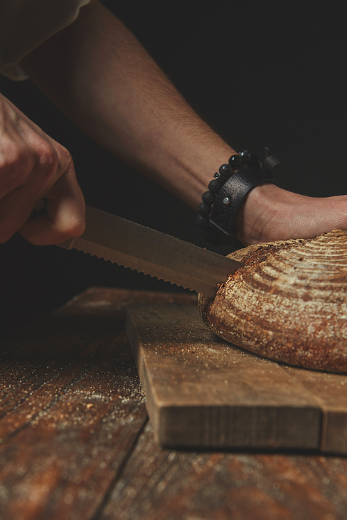 The man cuts fresh rustic bread on a wooden background