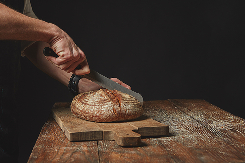 Baker slicing tasty fresh Rye grain bread. Healthy eating concept