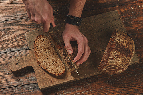 Rye grain bread put on kitchen wood board , chef holding gold knife for cut.