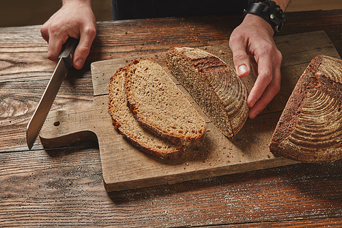 Man slicing tasty fresh Rye grain bread. Healthy eating concept