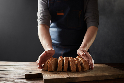Baker's hands with a bread. Chef hand cutting homemade bread sliced. Rustic dark styling