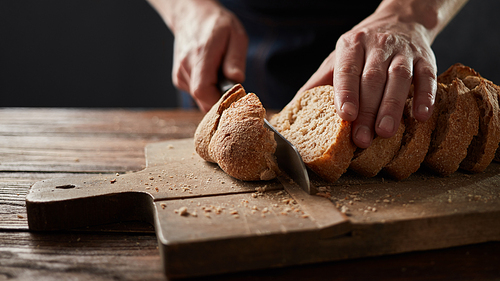 Hand cuts freshly baked bread on a cutting board . Close up. The healthy eating and traditional bakery concept