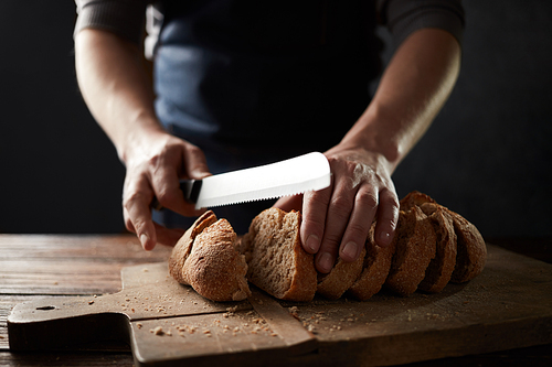 Whole grain bread put on kitchen wood plate with a chef holding knife for cut. Fresh bread on table close-up. The healthy eating and traditional bakery concept