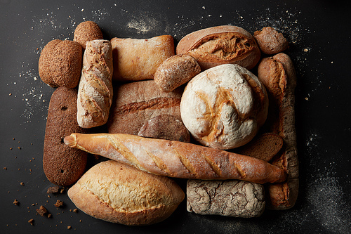 Different kinds of bread represented over black background. Fresh bread after baking: white and brown bread. Collection of wholegrain, sesame, grain, etc. bread. Bakery concept.