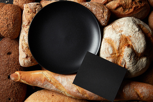 variety of breads like a frame and a black plate inside with a place under the text, flat lay