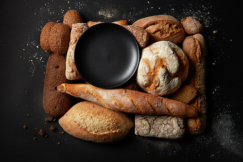 Fresh baked bread background, variety of different kind of breads, food industry. Top view of plate represented among different kinds of breads. Different bread sorts.