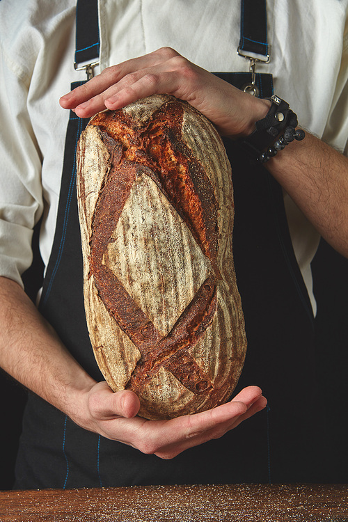 Close up hands man holding an oval fresh bread on a background