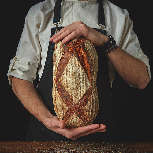 On a black background the hands man holding a fresh dark homemade bread