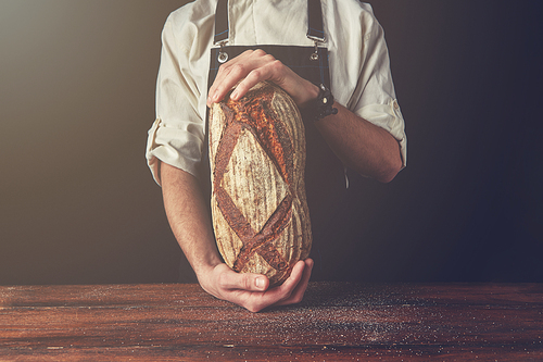 Man's hands hold fresh rye bread from whole grains on the black background of a wooden table , tonned photo
