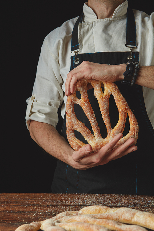 In the hands of a baker organic fresh fougas bread on a dark background