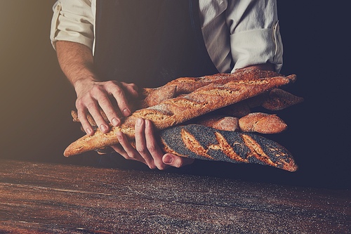 Freshly baked baguettes hold a man's hands against a background of a wooden table, tonned photo