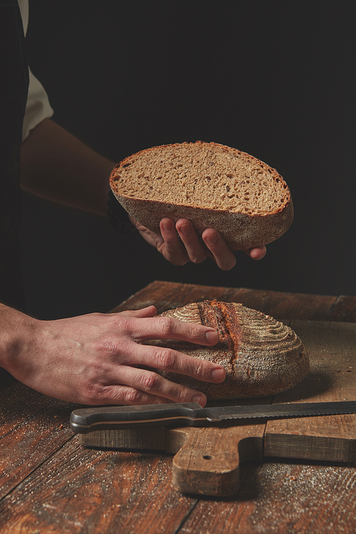 Hands keeping loaf of baked bread on dark background