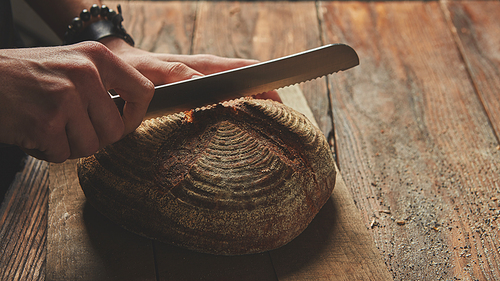 Hands of a man cutting fresh rye bread on a wooden background