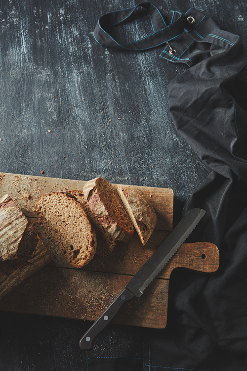 Knife, bread sliced on a wooden board On a dark background flat lay