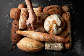 Baking and cooking concept background. Top view of different bread sorts with woman's hand adjusting them. Bread on black table sprinkled with flour.