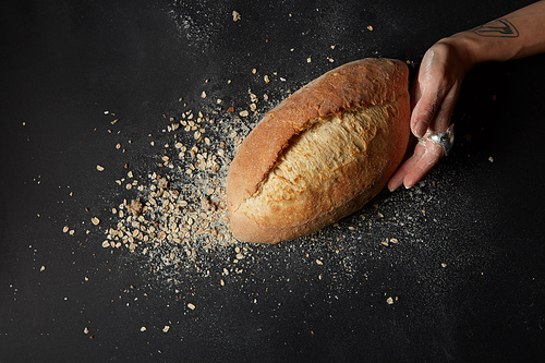 hand in flour holds a fresh bread against the flakes on dark background