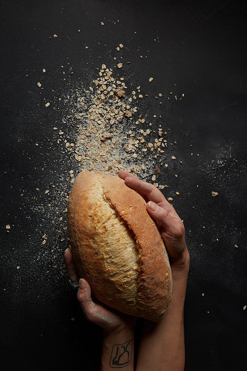 Baker's hands with a bread with flakes on a black background