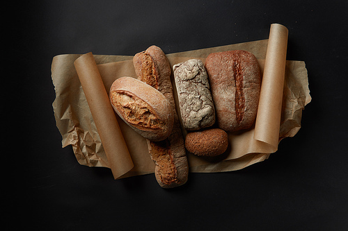 Mix fresh bread on parchment on black background in still life.