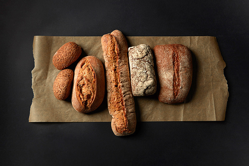 Different kinds of loafs represented on baking paper over black background. Baking and cooking concept background.