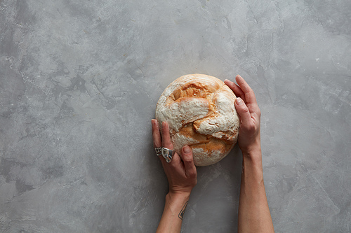 Baker man holding a beautiful round bread on a gray stone background