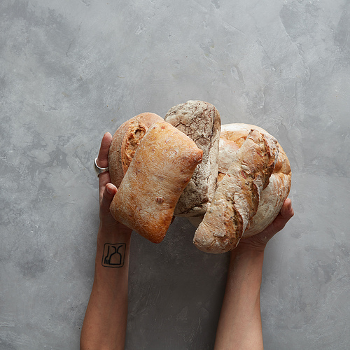 Lots of different bread sorts in the hands of a baker on a gray background, Baking and cooking concept background.