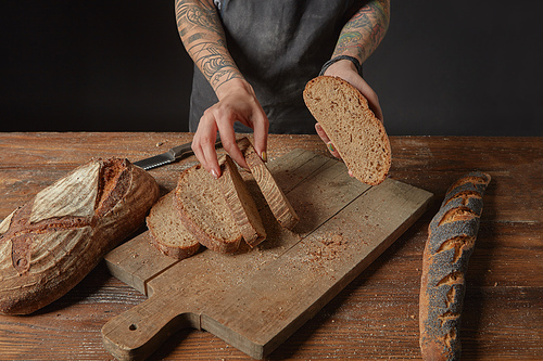 Woman with tattoos on her hands slicing grain bread on a wooden board