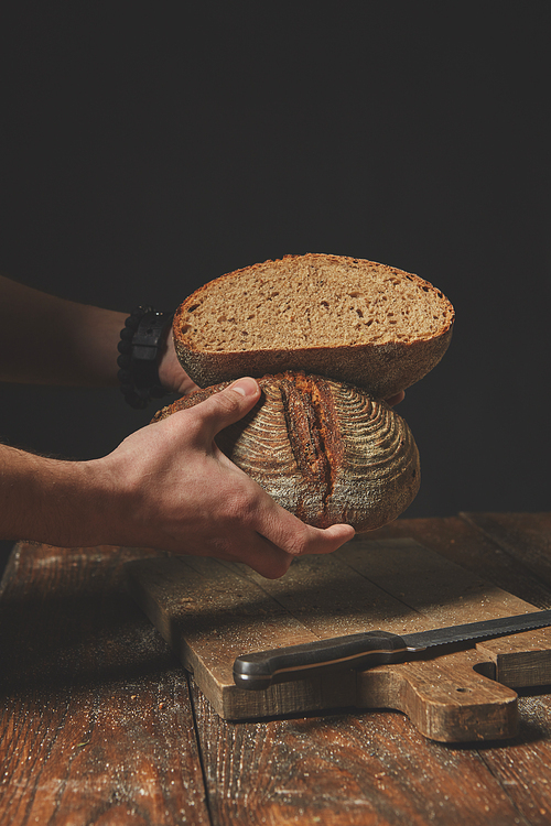 Men's hands hold two halves of rye bread on a dark background