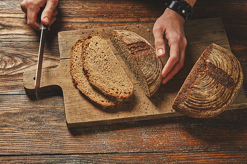 Sliced bread on a wooden brown board with man's hand holds a knife flat lay
