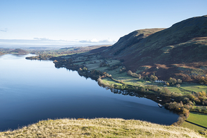 Epic Autumn Fall landscape of Ullswater and surrounding mountains and hills viewed from Hallin Fell on a crisp cold morning with stunning sunlgiht hitting the slopes