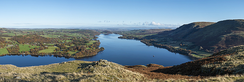 Epic Autumn Fall landscape of Ullswater and surrounding mountains and hills viewed from Hallin Fell on a crisp cold morning with stunning sunlgiht hitting the slopes