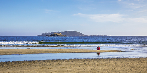 View of woman with hat and red shirt sitting alone at the beach staring at the sea