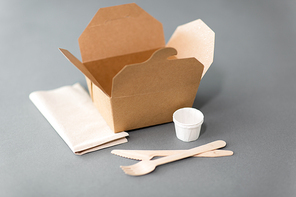 package, recycling and eating concept - disposable box for takeaway food with wooden fork, knife and napkin on table
