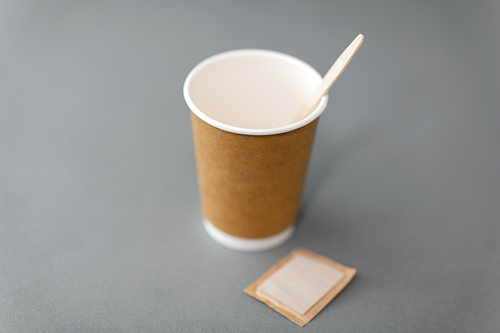 dispose, recycling and ecology concept - takeaway paper coffee cup with spoon and sugar bag on grey background