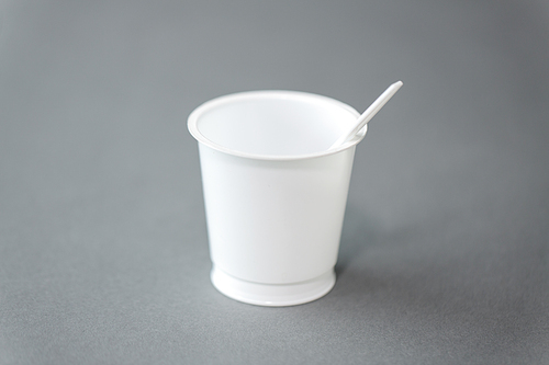 eating, recycling and ecology concept - white disposable plastic cup with spoon on grey background