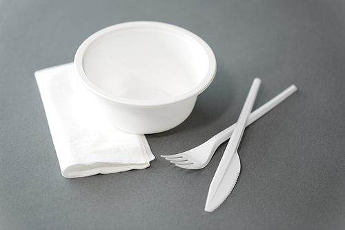 eating, recycling and ecology concept - white disposable plastic plate with fork, knife and paper napkin on grey background