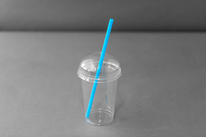 dispose, recycling and ecology concept - transparent takeaway plastic cup with straw on grey background