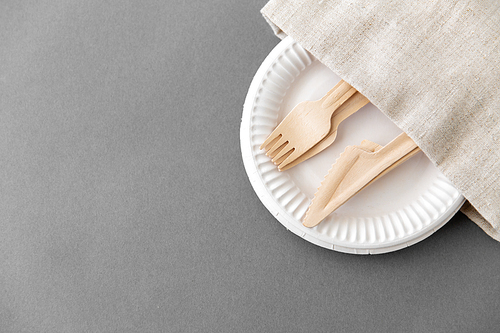cutlery, recycling and eco friendly concept - wooden forks and knives on paper plates and canvas napkin on grey background