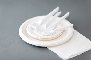 eating, recycling and ecology concept - disposable paper plates and plastic spoons, knives and forks on grey background