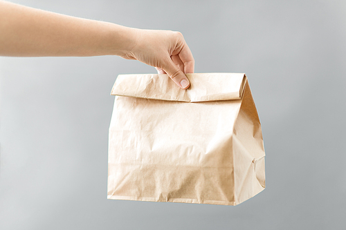 recycling and ecology concept - hand holding disposable brown takeaway food in paper bag with lunch on table