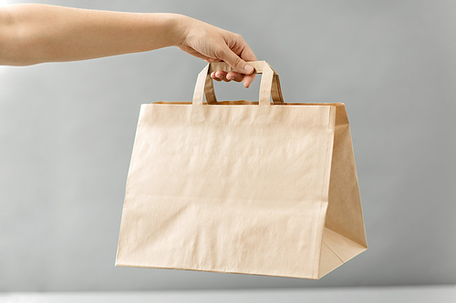 recycling, shopping and ecology concept - hand holding disposable brown takeaway food in paper bag with lunch on table